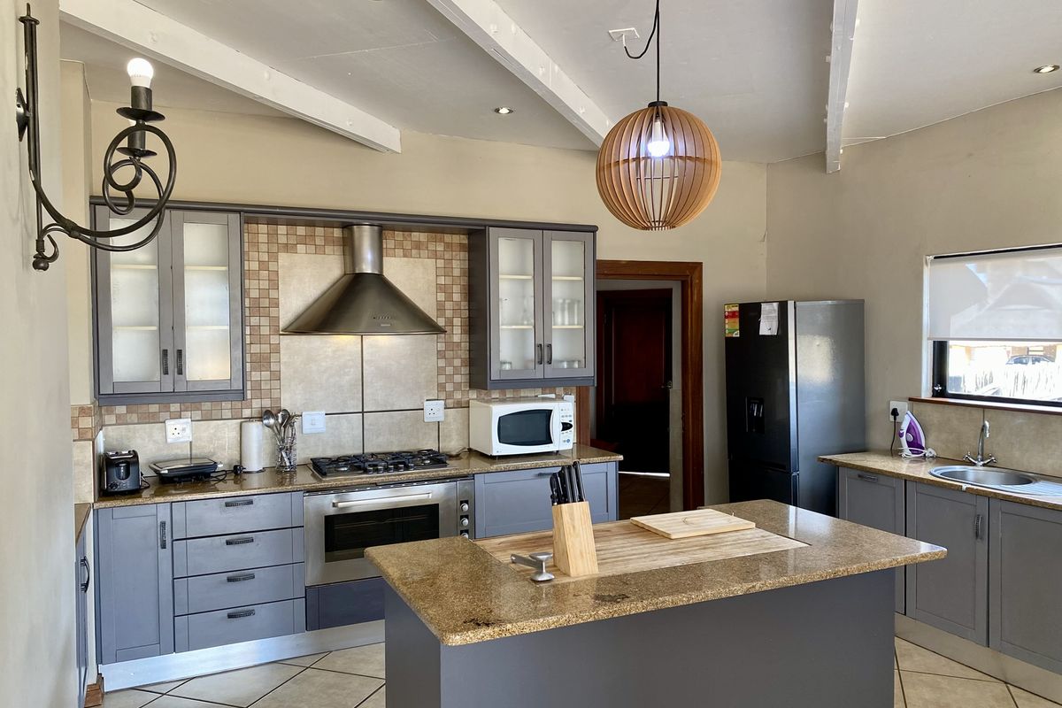 Modern kitchen featuring grey cabinetry, granite countertops, a central island, stainless steel gas hob, extractor fan, and tiled flooring with exposed ceiling beams.