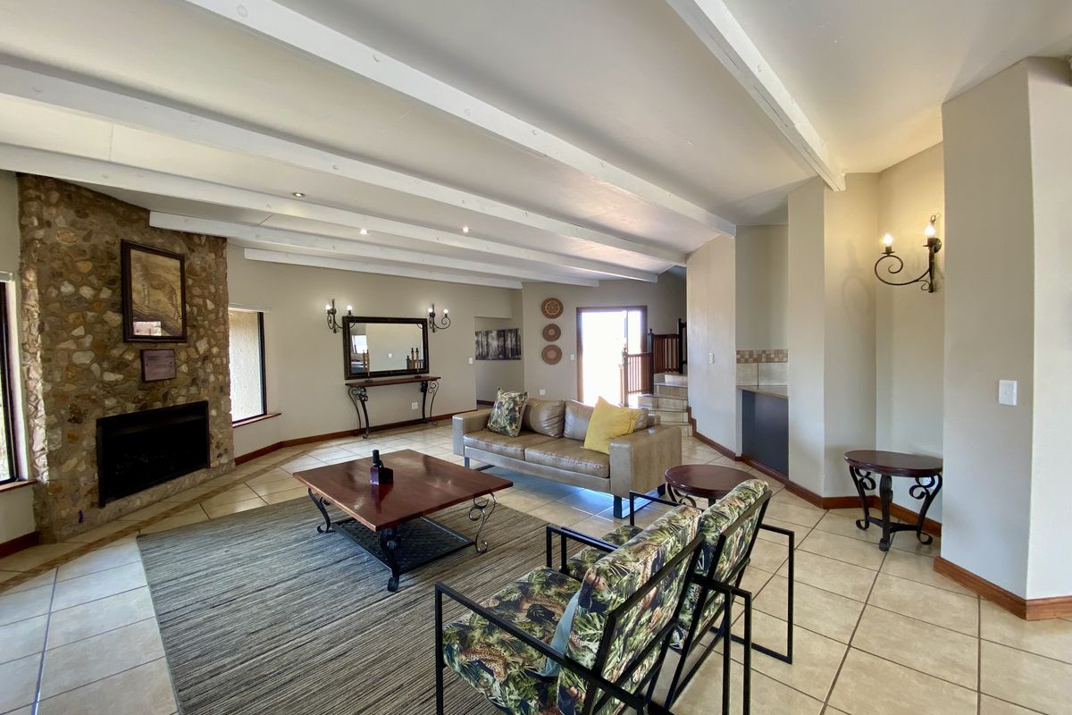 Spacious living room featuring a prominent stone-clad fireplace, exposed ceiling beams, and tiled flooring, creating a warm and inviting atmosphere.