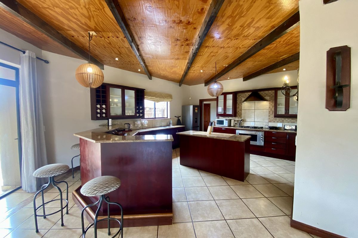 Spacious kitchen featuring dark wood cabinetry, a central island, granite countertops, and a vaulted timber-paneled ceiling with exposed beams.