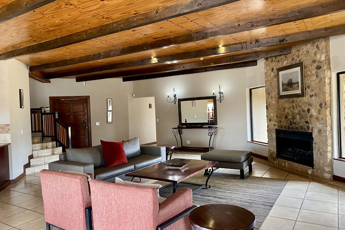 Spacious living room featuring exposed timber ceiling beams, a prominent stone-clad fireplace, and tiled flooring throughout.