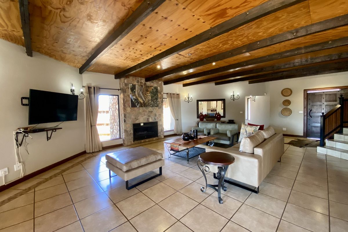 Spacious living room featuring a prominent stone-clad fireplace, exposed timber ceiling beams, and large ceramic floor tiles.