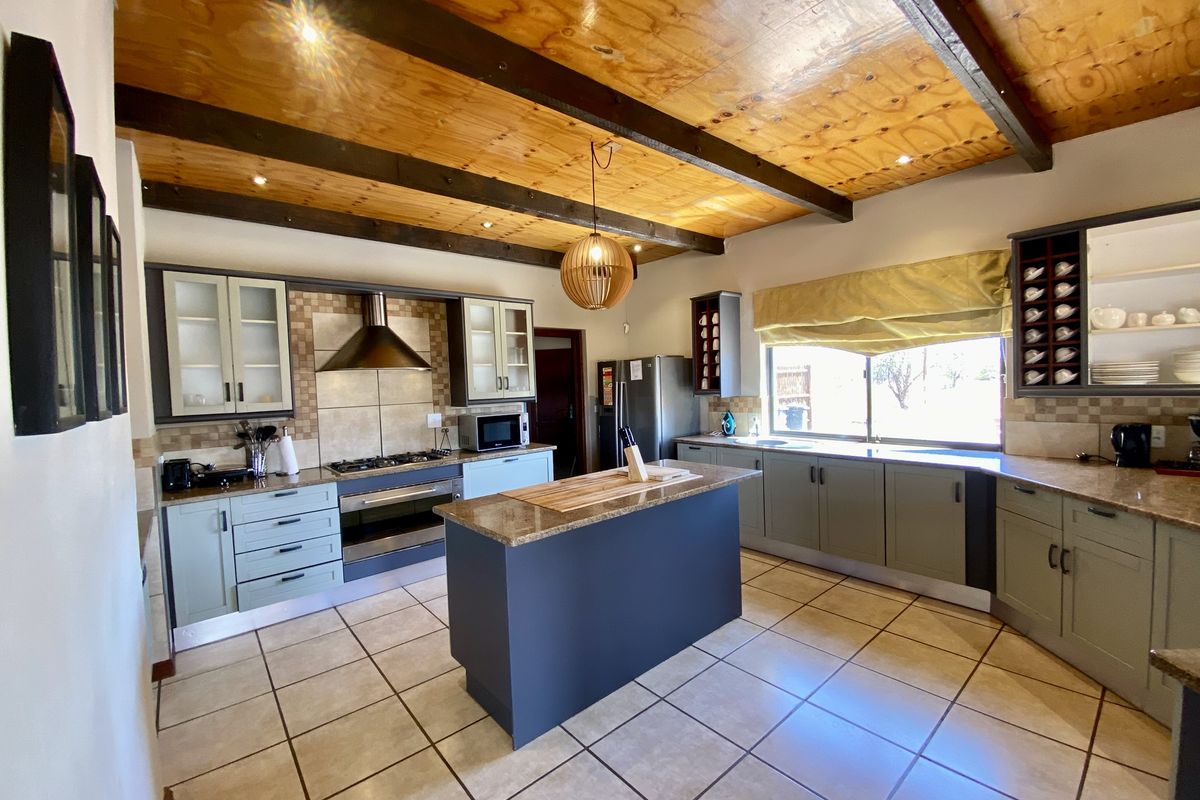 Spacious kitchen featuring a central island, granite countertops, built-in oven, gas hob, extractor fan, and exposed timber ceiling beams.
