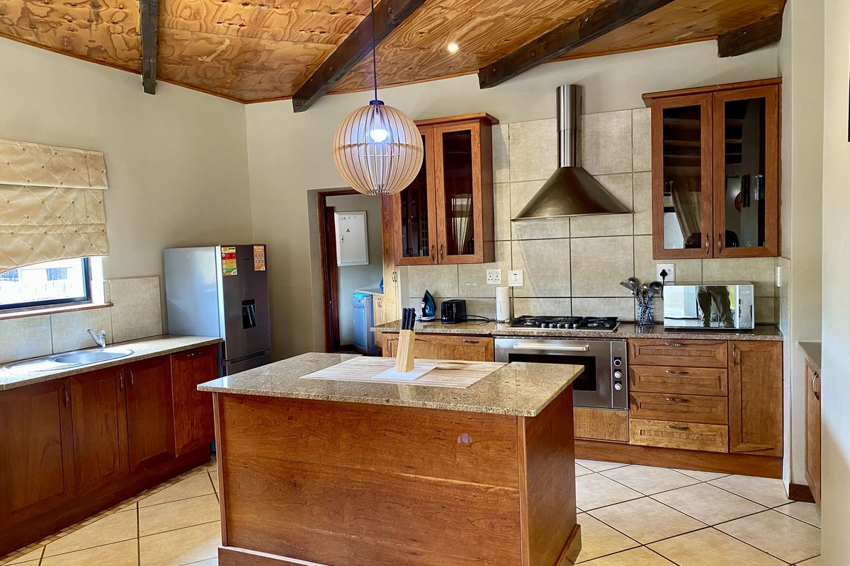 A spacious kitchen featuring wooden cabinetry, a central island with granite countertops, a built-in oven, gas hob, and a distinctive vaulted timber ceiling.