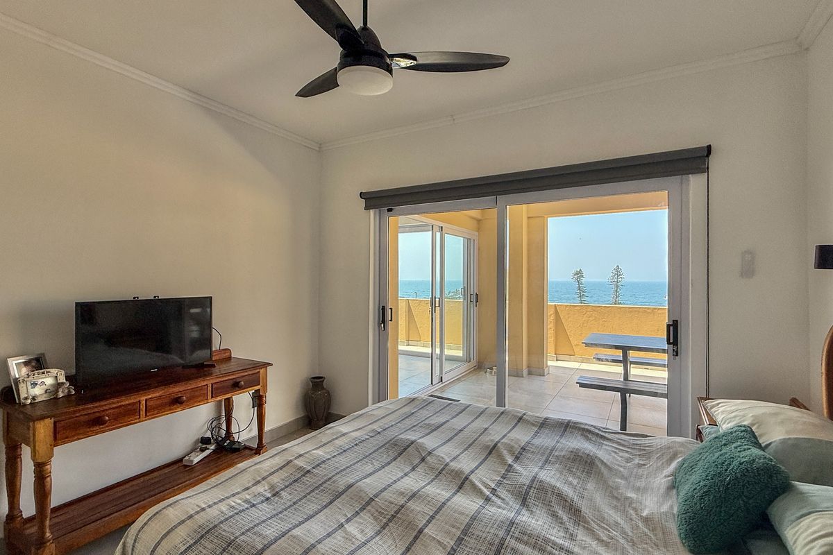 Bedroom featuring a ceiling fan and sliding glass doors that open onto a private balcony with ocean views.