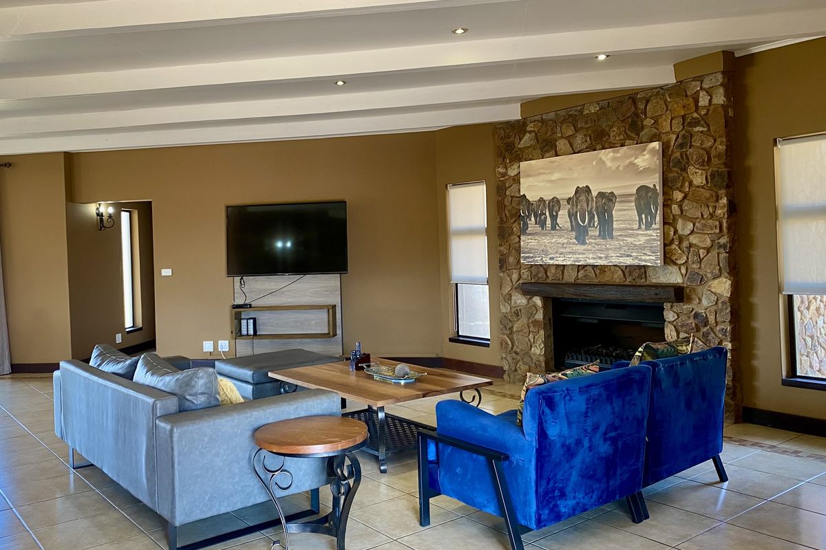 Spacious living room featuring a prominent stone-clad fireplace, tiled flooring, exposed ceiling beams, and recessed lighting.