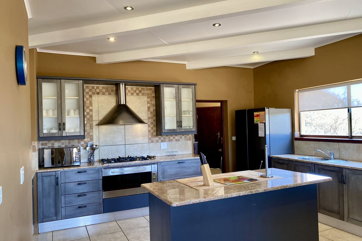 A well-appointed kitchen featuring dark cabinetry, granite countertops, a central island, stainless steel extractor fan, and built-in oven with gas hob.