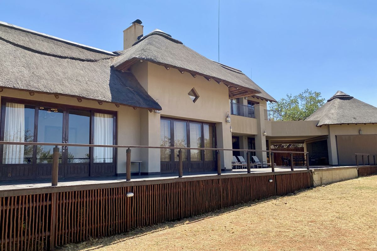 Spacious rear exterior view featuring a large raised timber deck, thatched roof architecture, and expansive glass sliding doors leading into the home.