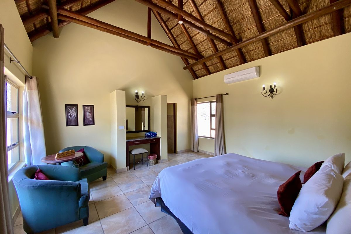 Spacious bedroom featuring a high vaulted thatched ceiling with exposed timber beams, tiled flooring, and an integrated air conditioning unit.