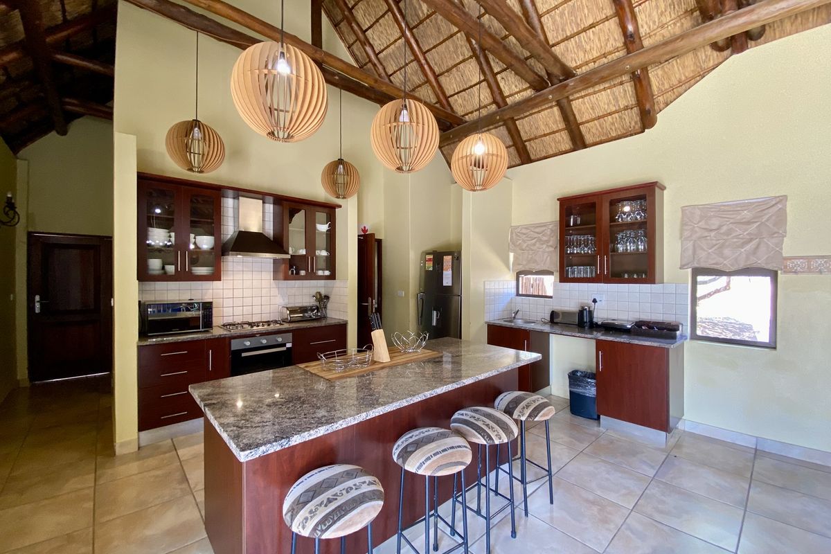 Spacious kitchen featuring dark wood cabinetry, granite countertops, a central island, and a high vaulted thatched ceiling with exposed timber beams.