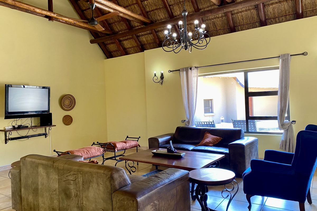 Spacious living room featuring a high vaulted thatched ceiling with exposed timber beams, tiled flooring, and large windows providing natural light.