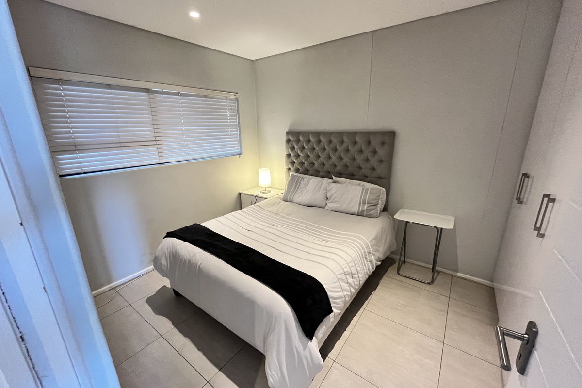 A well-maintained bedroom featuring neutral tiled flooring, built-in cupboards, and horizontal window blinds, offering a clean and functional living space.