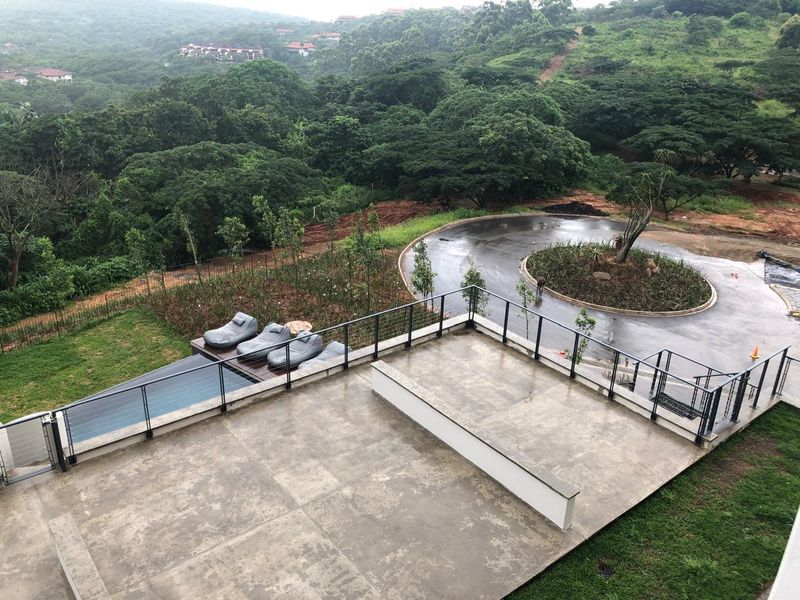 Spacious elevated patio area featuring a modern metal railing, overlooking a swimming pool and lush green landscape with a circular driveway.