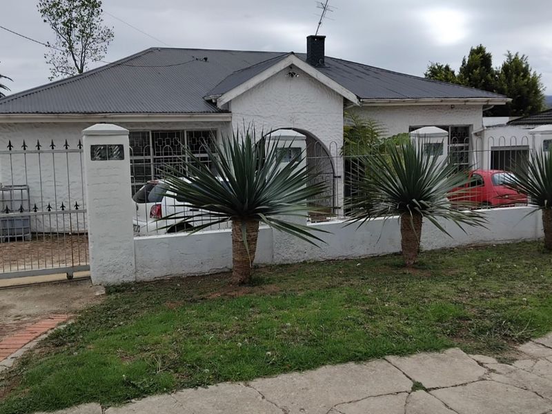 Front elevation of a single-story house featuring a metal roof, white painted brick facade, and a secure gated entrance with a front garden.