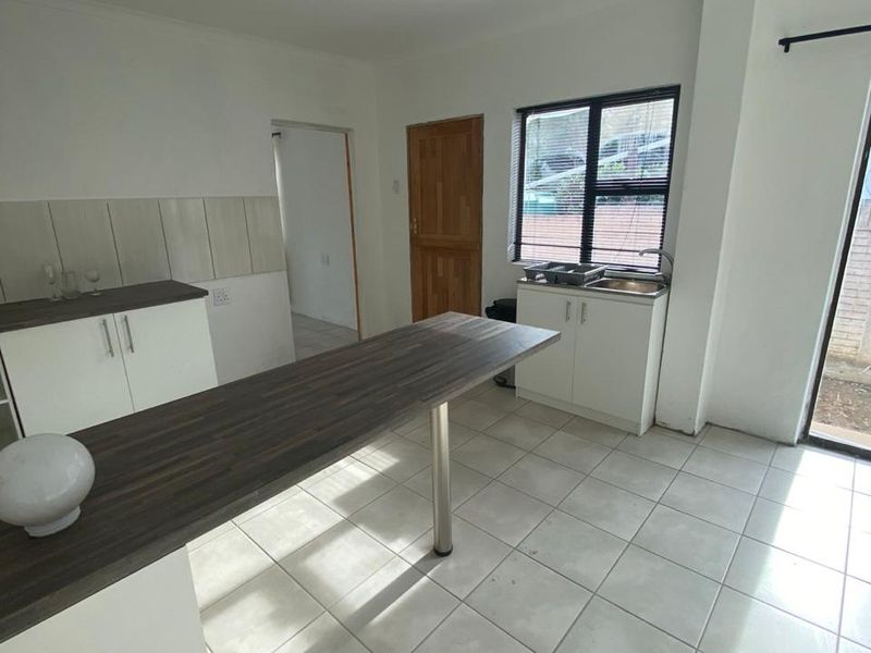 A functional kitchen area featuring built-in cabinetry, a breakfast bar, tiled flooring, and direct access to the exterior.