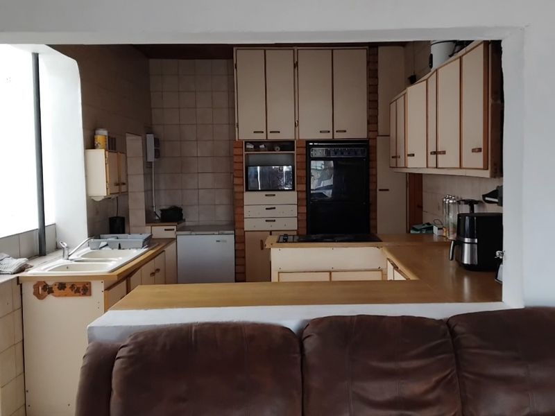 A dated kitchen featuring built-in cabinetry, laminate countertops, and integrated oven, viewed from the adjacent living area through a service opening.
