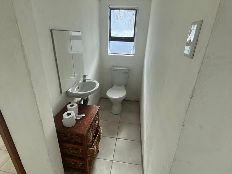 A compact bathroom featuring a wall-mounted basin, toilet, and tiled flooring, requiring cosmetic updates to improve the overall finish and aesthetic.