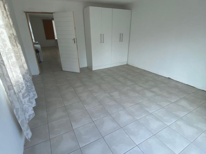 A simple, vacant bedroom featuring neutral tiled flooring and a built-in wardrobe, offering a clean canvas for personalization.