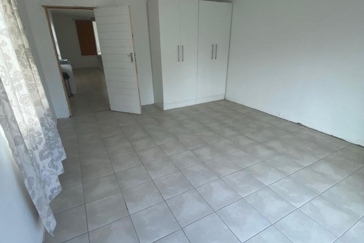 A simple, vacant bedroom featuring neutral tiled flooring and a built-in wardrobe, offering a clean canvas for personalization.