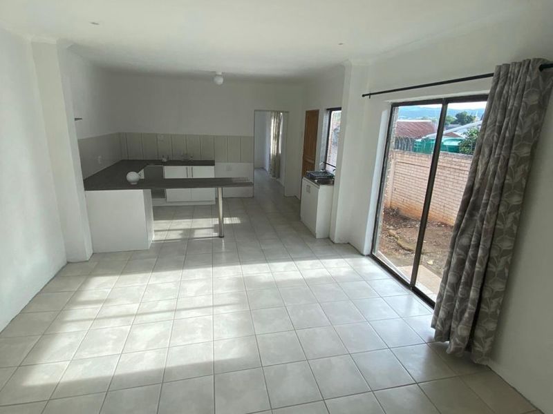 An open-plan living and kitchen area featuring neutral tiled flooring, built-in cabinetry, and a sliding glass door providing access to the exterior.