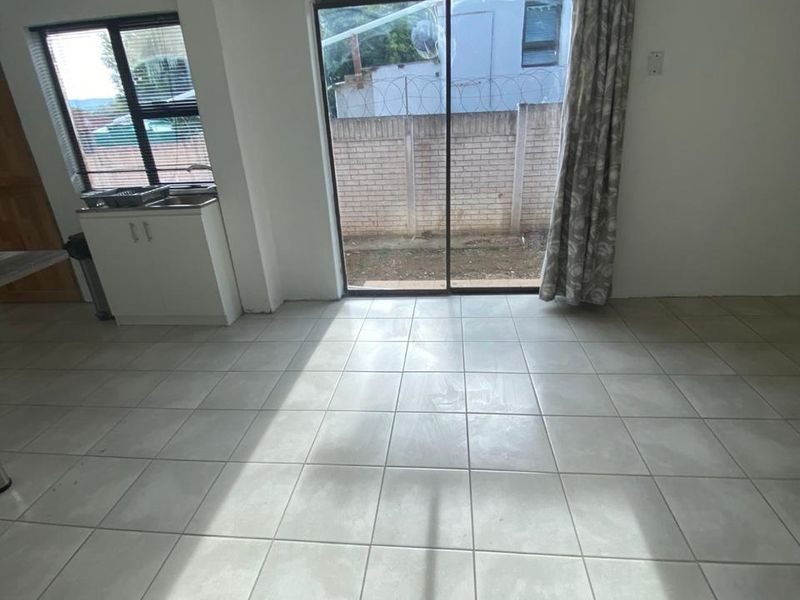 An open-plan living area featuring neutral tiled flooring, a built-in sink cabinet, and a sliding glass door providing access to the rear exterior.