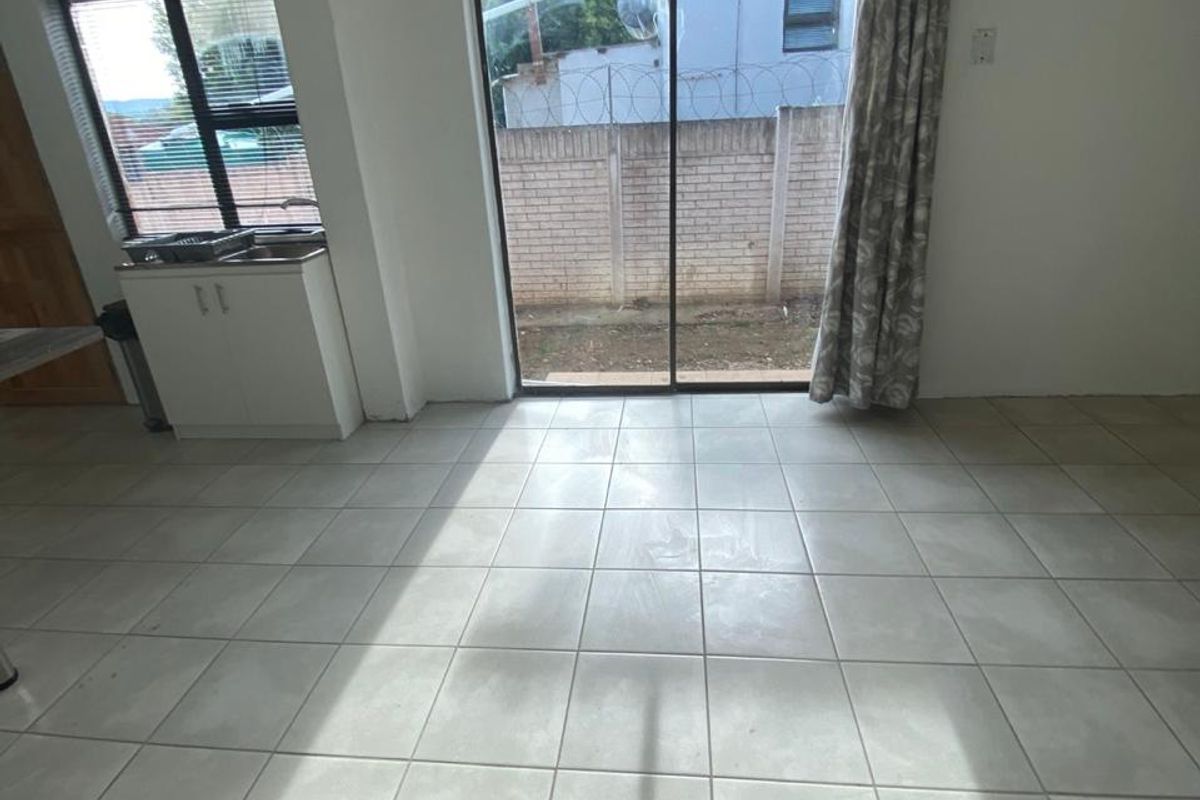 An open-plan living area featuring neutral tiled flooring, a built-in sink cabinet, and a sliding glass door providing access to the rear exterior.