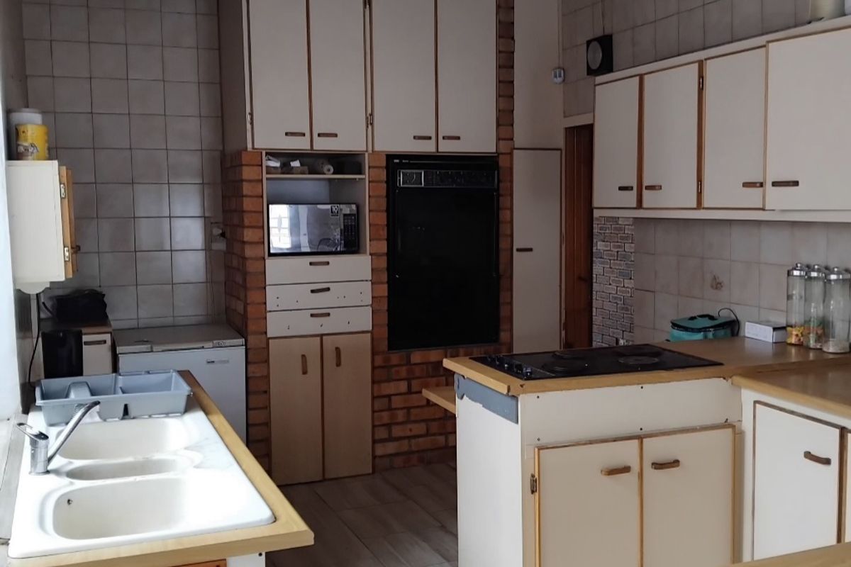 A dated kitchen featuring built-in cabinetry, a double basin sink, integrated oven, and electric hob with a brick feature wall and tiled backsplash.