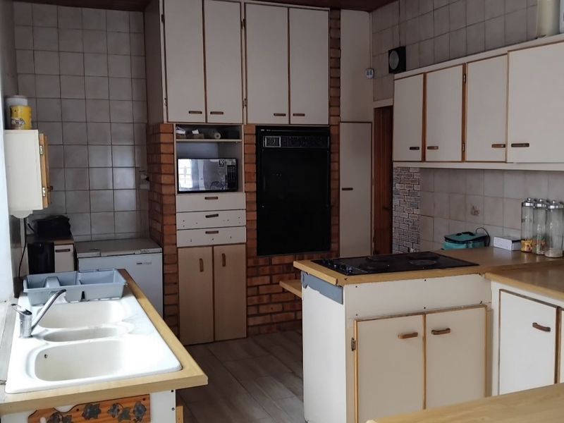 A dated kitchen featuring built-in cabinetry, a double basin sink, integrated oven, and electric hob with a brick feature wall and tiled backsplash.