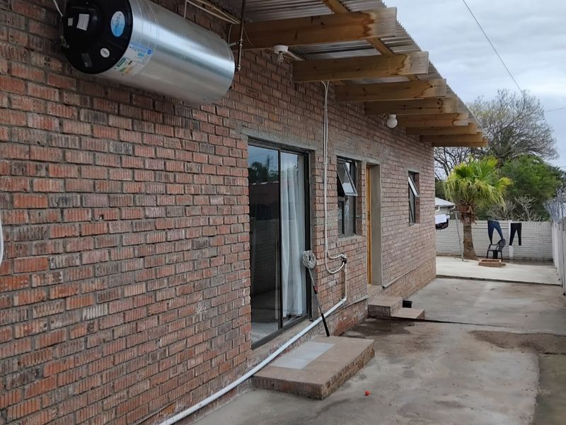 Rear exterior view of a brick house featuring a corrugated metal roof, exposed timber rafters, and an externally mounted electric water heater.
