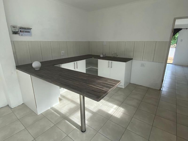A basic, empty kitchen area featuring laminate countertops, built-in cabinetry, a breakfast bar, and tiled flooring, offering a blank canvas for renovation.