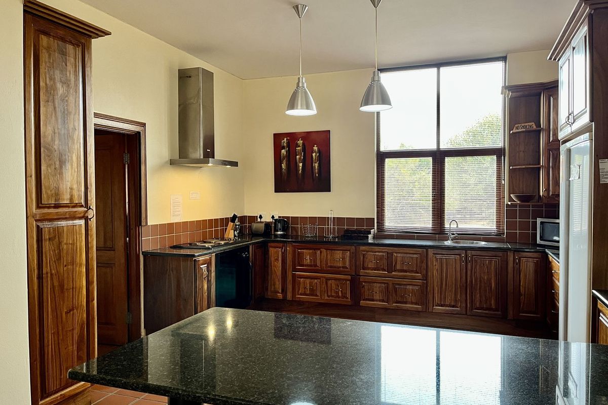 Spacious kitchen featuring dark wood cabinetry, granite countertops, a central island, stainless steel extractor fan, and large windows providing natural light.