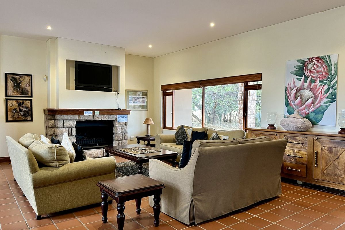 Spacious living room featuring a stone-clad fireplace, large windows with garden views, and terracotta tile flooring.