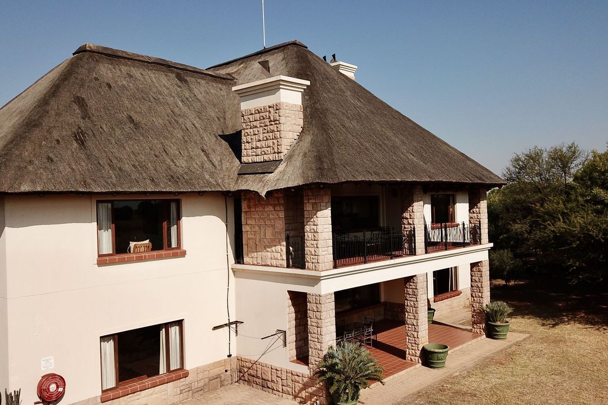 An elevated view of a two-story house featuring a traditional thatched roof, stone-clad pillars, and a spacious covered patio area.