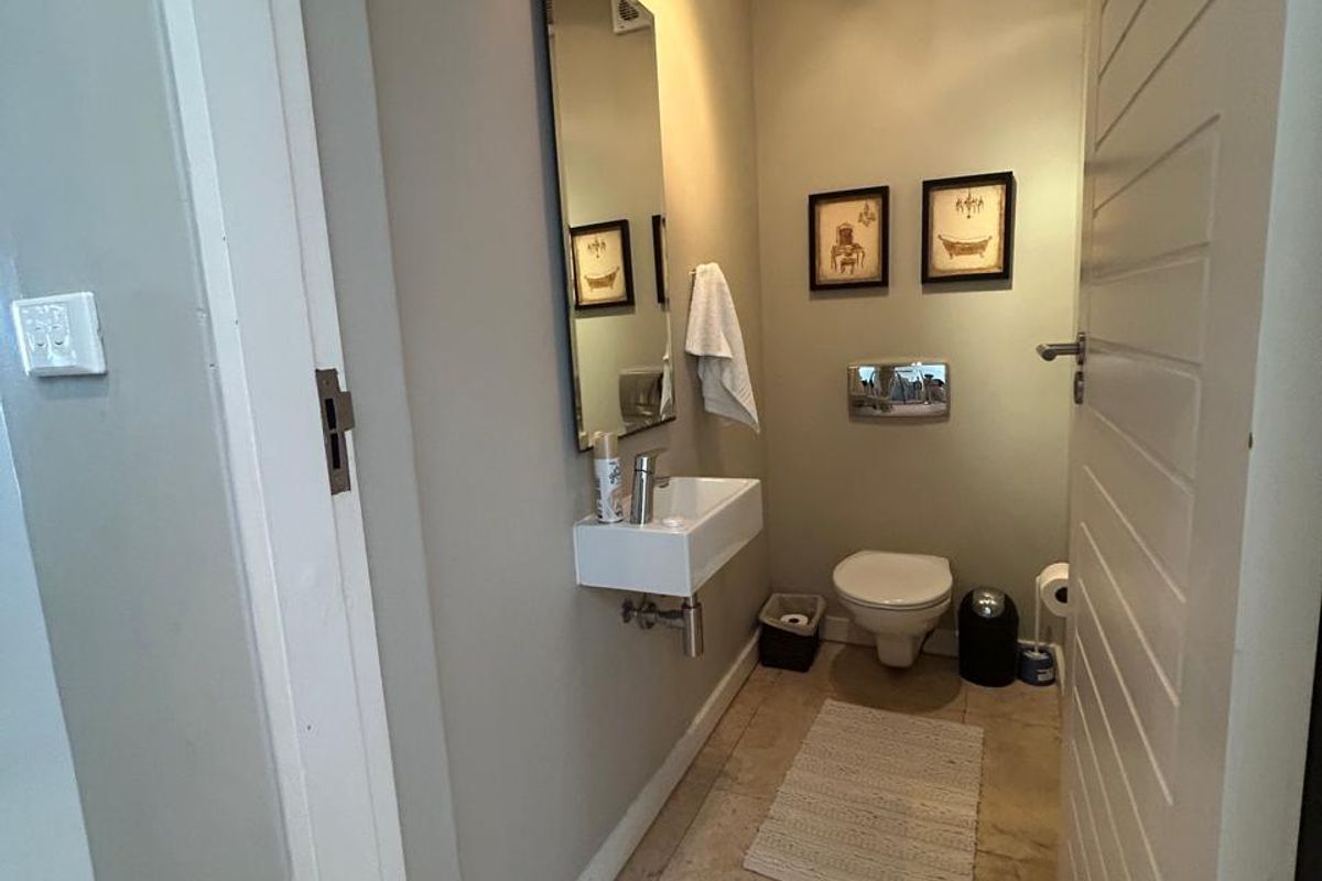 A compact guest bathroom featuring a wall-mounted basin, toilet, and neutral tiled flooring.
