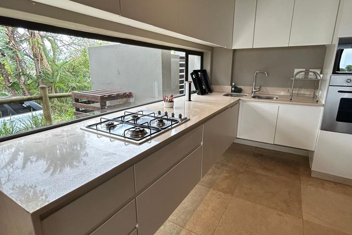 Modern kitchen featuring sleek handleless cabinetry, stone countertops, a gas hob, built-in oven, and large horizontal window overlooking the exterior.
