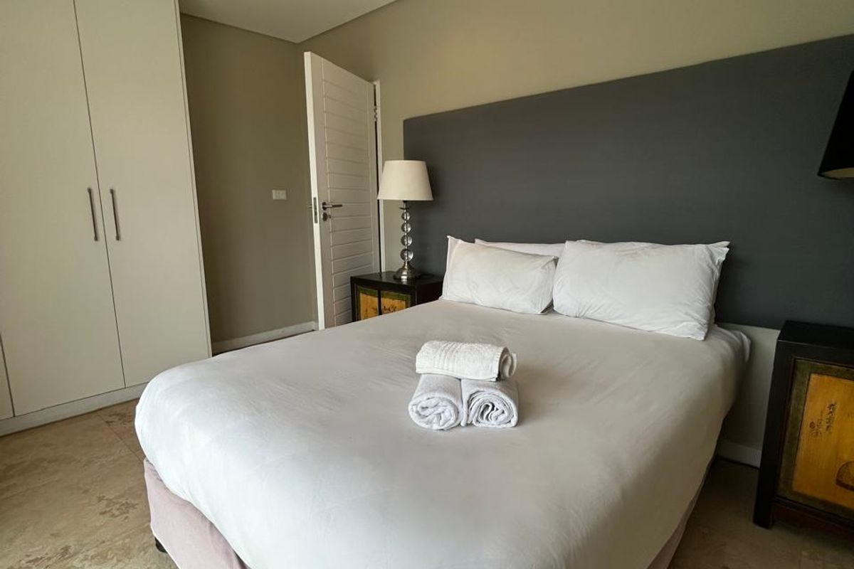 A well-maintained bedroom featuring neutral wall tones, built-in white cabinetry, recessed ceiling lighting, and polished stone flooring.