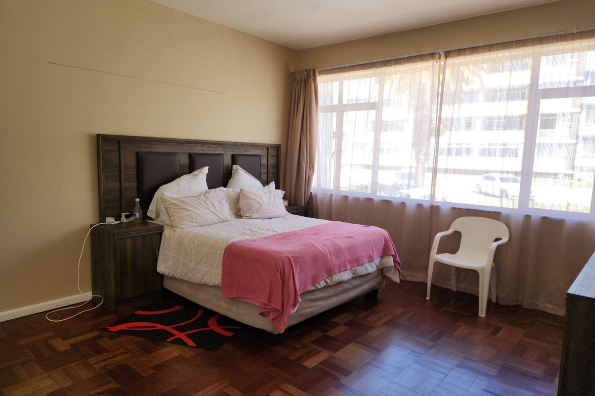A bedroom featuring classic parquet flooring and a large window allowing natural light, with some visible wall surface imperfections requiring attention.