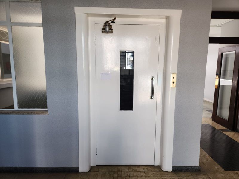 A functional elevator entrance located in a communal hallway with a white metal door and integrated call panel.