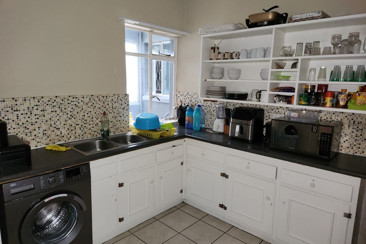 Functional kitchen featuring white cabinetry, mosaic tile backsplash, double basin sink, and open shelving, providing a practical layout for daily use.