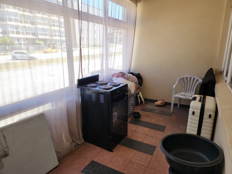 Enclosed balcony area featuring large windows, tiled flooring, and a freestanding electric stove, offering potential for a functional utility or sunroom space.