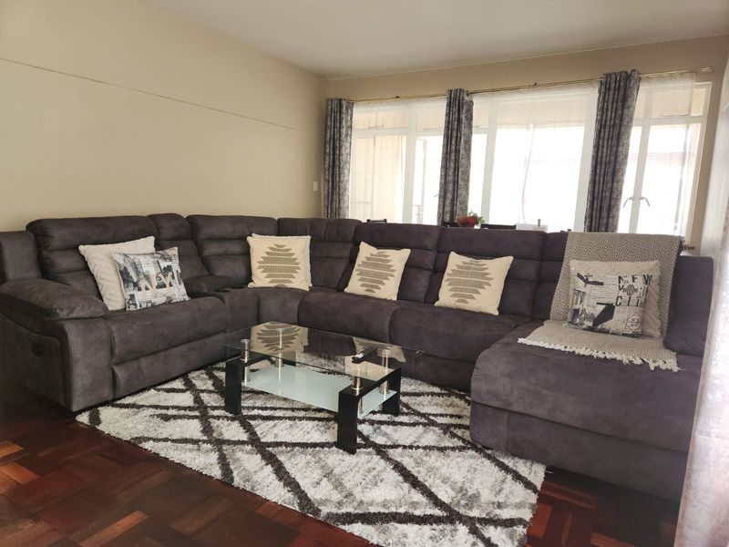A spacious living room featuring warm parquet flooring and large windows that allow for ample natural light.