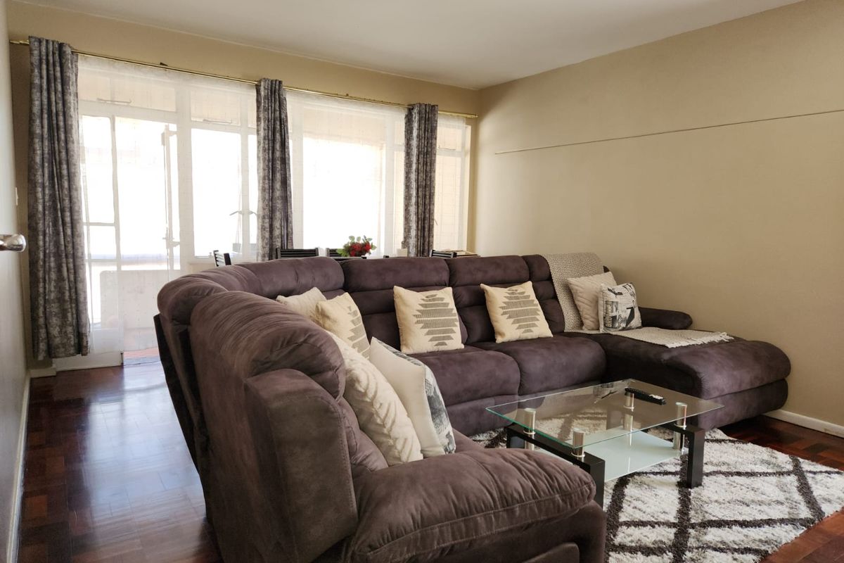 A spacious living room featuring warm parquet flooring and a large glass sliding door that provides ample natural light and access to the balcony.