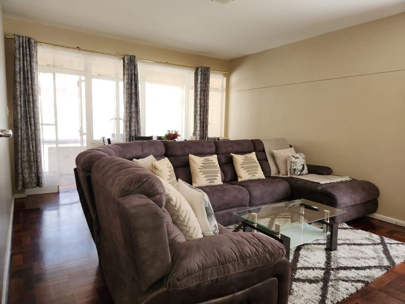 A spacious living room featuring warm parquet flooring and a large glass sliding door that provides ample natural light and access to the balcony.