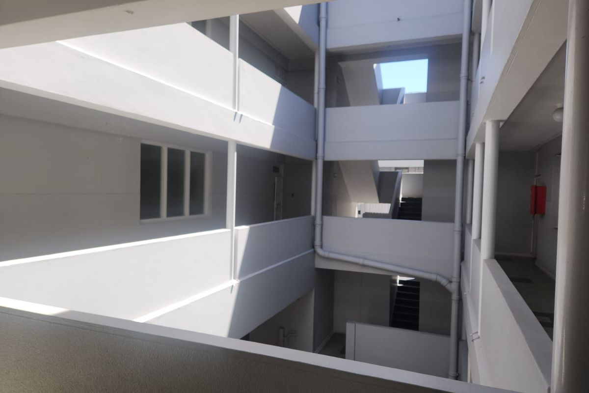An open-air apartment building atrium featuring concrete walkways, staircases, and external plumbing infrastructure.