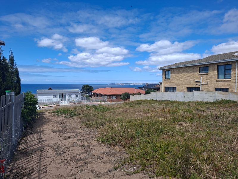 A vacant residential plot featuring natural ground cover, enclosed by a precast concrete wall and metal fencing, offering distant ocean views.