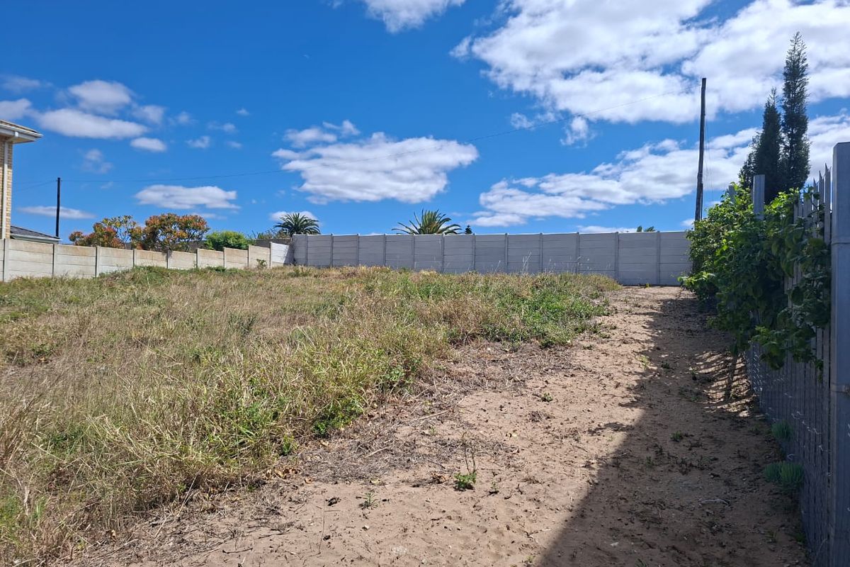 A vacant residential plot featuring a sandy surface, overgrown grass, and secure precast concrete boundary walling.