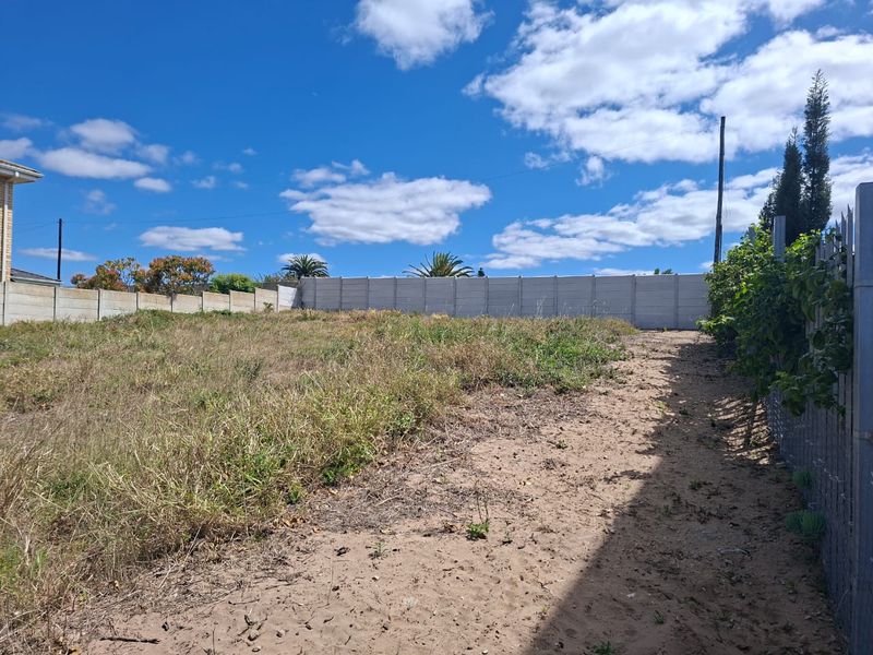 A vacant residential plot featuring a sandy surface, overgrown grass, and secure precast concrete boundary walling.