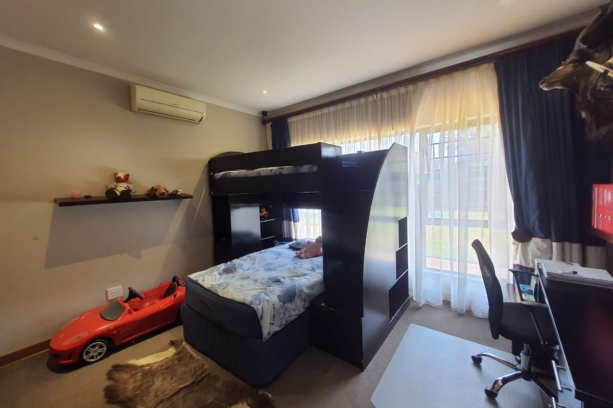 A bedroom featuring carpeted flooring, recessed ceiling lighting, and a wall-mounted air conditioning unit, with large windows providing natural light.