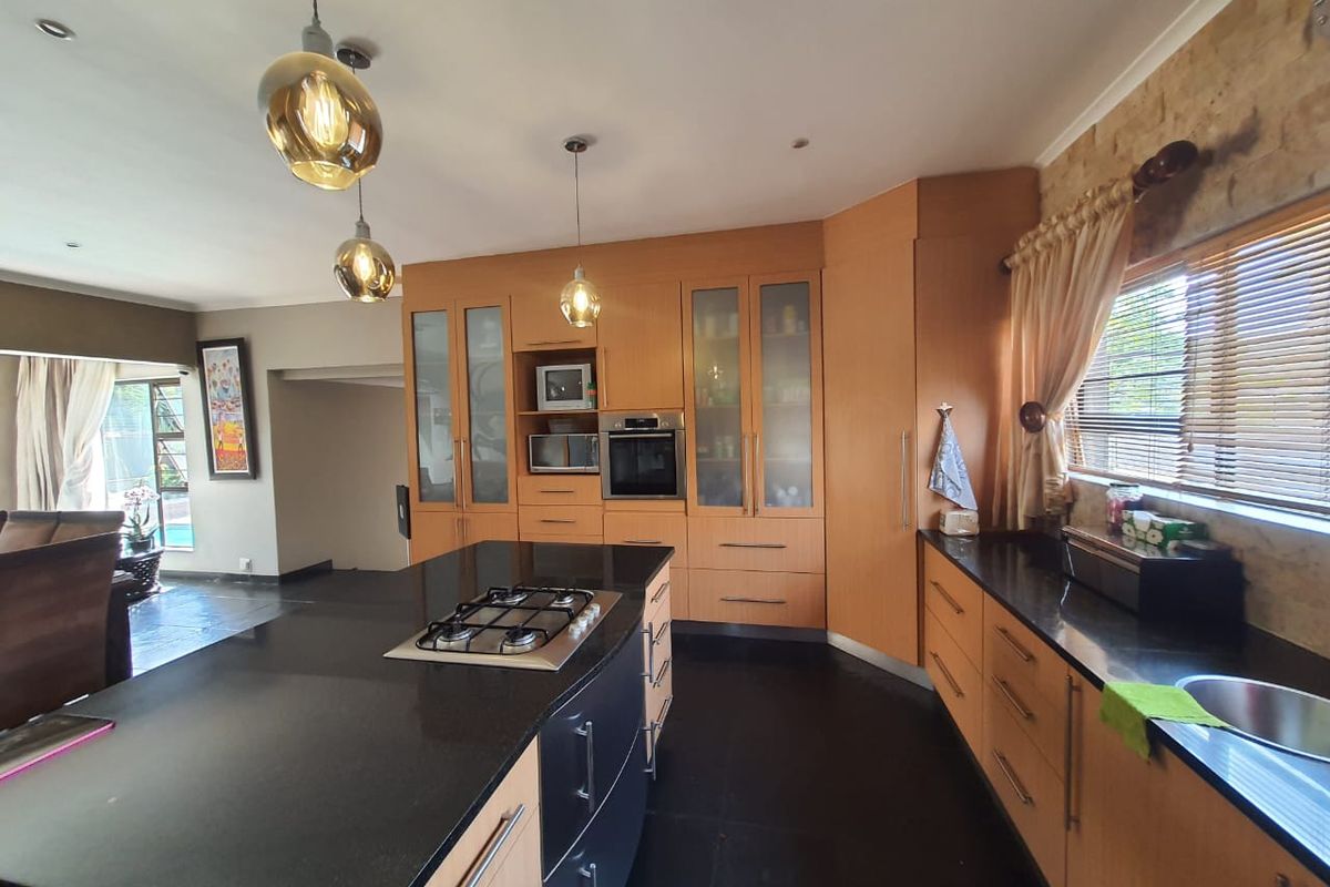 Modern kitchen featuring light wood cabinetry, black granite countertops, a central island with a built-in gas hob, and integrated oven and microwave.