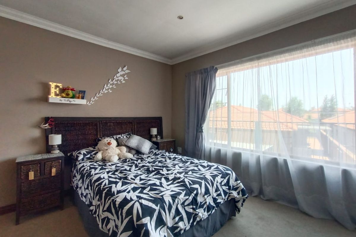 A well-lit bedroom featuring neutral wall tones, carpeted flooring, and a large window with sheer curtains providing natural light.