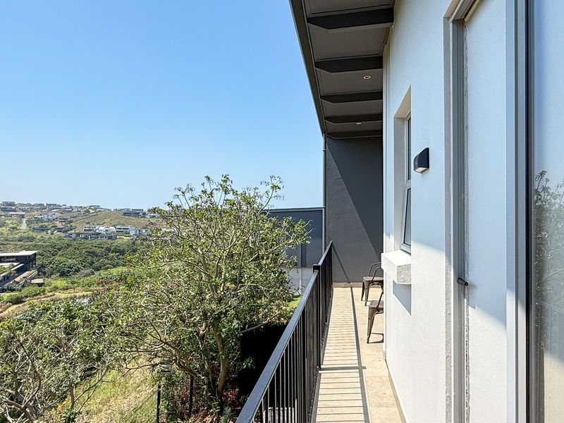 A modern balcony featuring a metal balustrade, tiled flooring, and recessed lighting, offering expansive views of the surrounding landscape.